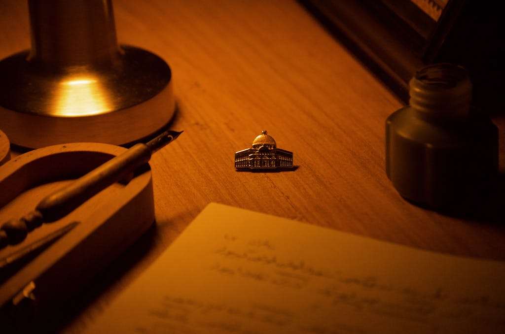 Warm-toned desk scene with lamp, ink pot, and decorative object.